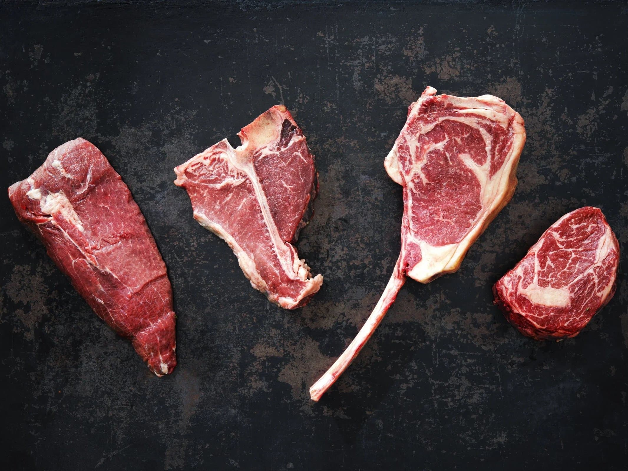 Beef steaks arranged on a dark slate surface