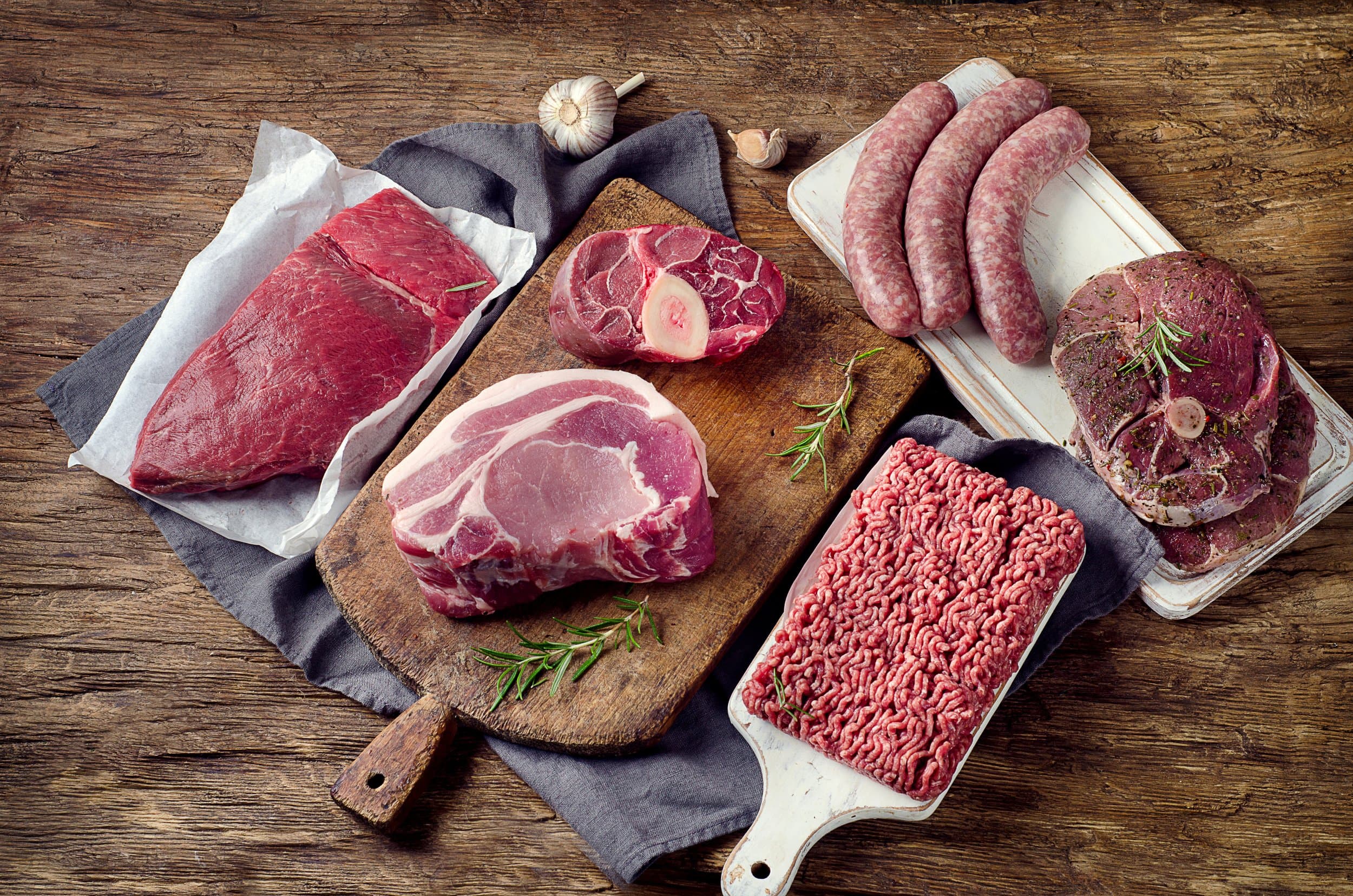 An assortment of beef and pork cuts, sausages and ground meat on a wooden table